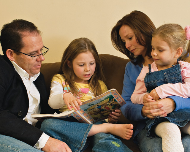 A photo of a Mormon family gathered together on a couch to read a Family Home Evening lesson.