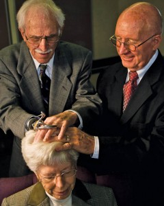 A photo of two elderly men giving a blessing to an elderly woman by the laying on of hands.