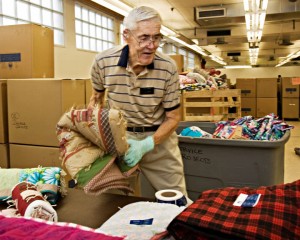 A photo of an elderly man helping fold and pack quilts for a service project.