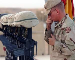 A soldier stands next to a memorial for fallen soldiers.