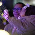 A father and daughter look at lights on a Christmas tree.