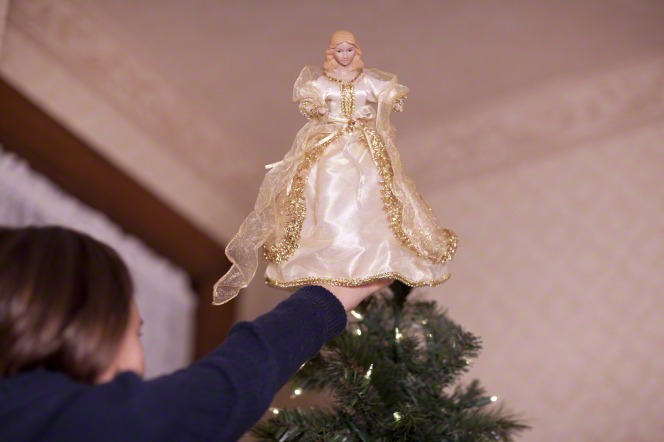 A girl puts an angel on the Christmas tree. We can add our light to the world by serving others this season.