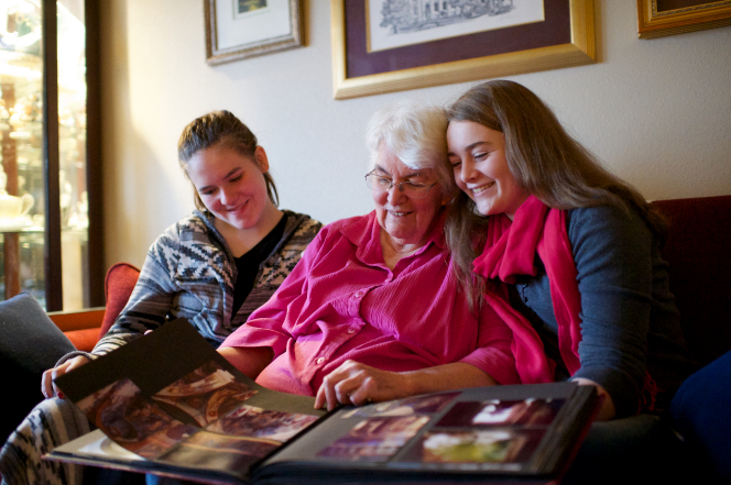 Young women sitting with their grandmother looking at family pictures.